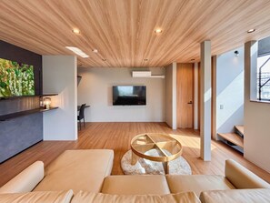 Un soggiorno moderno con televisione a schermo piatto, soffitto in legno e un tavolino da caffè rotondo in vetro.