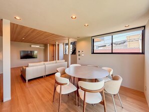 Un salon moderne comprenant un téléviseur, un canapé, une table à manger avec des chaises et une grande fenêtre donnant sur un beau paysage.