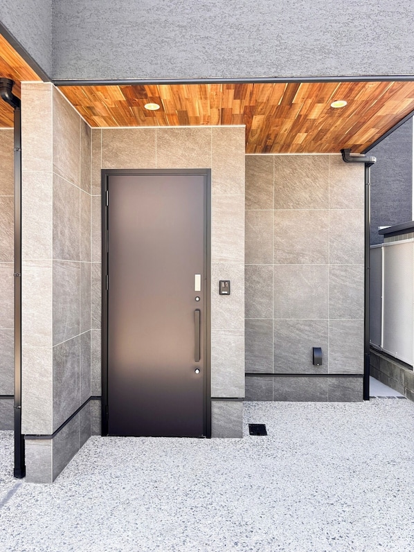 A modern building entrance with a dark door, tiled walls, and a wooden ceiling.