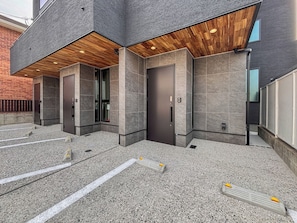 A modern building with a mix of concrete and wood elements, large doors, and a paved ground.
