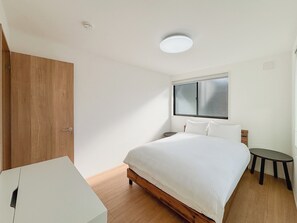 Une chambre à coucher avec un lit en bois, une table de chevet, une petite table ronde, une armoire et une fenêtre avec des stores.