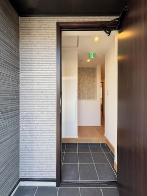 Un corridoio con una porta in legno, un muro di mattoni bianchi e un pavimento piastrellato.