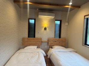 Une chambre avec deux lits, des têtes de lit en bois, un appareil de climatisation, une lampe fixée au mur et une fenêtre.