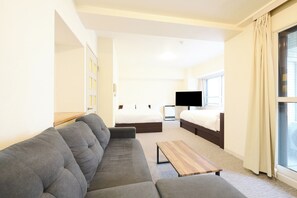 Et hotelværelse med sofa, seng, fjernsyn og et vindue med gardiner.