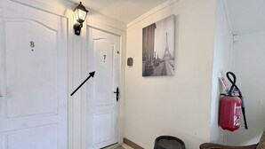 Un pasillo con una puerta blanca marcada '8', una puerta marcada '7', un extintor, un felpudo y una silla.