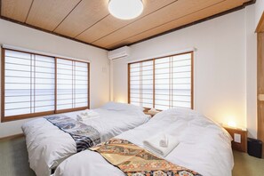 A room with two beds, wooden ceiling beams, large windows with grid patterns, and a bedside table with a lamp. - Fully renovated in 2025 Entire building for rent / Edogawa Ward Tokyo (Edogawa Ward)