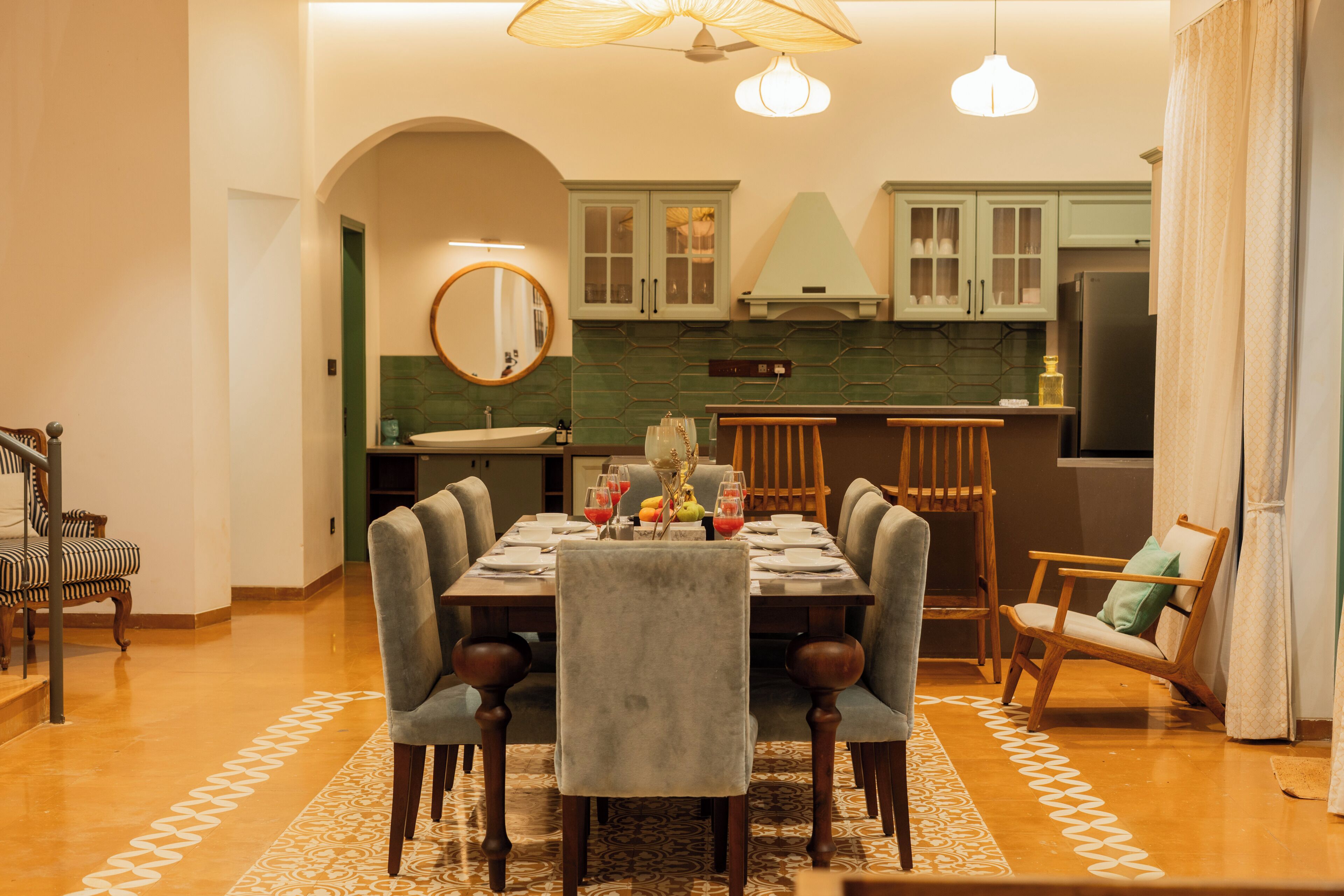 Un coin repas avec une table dressée pour six personnes, entourée de chaises, une cuisine en arrière-plan et un tapis à motifs sur le sol.