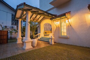Un patio cubierto con columnas, una escalera y una puerta con cortina.