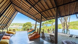A covered outdoor seating area with a view of a body of water and hills.