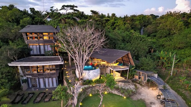 A modern multi-story building with a large tree in the center, surrounded by a well-maintained lawn and solar panels.