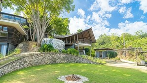 A modern house with a stone retaining wall, a large tree, and a grassy lawn.