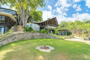 A modern house with a stone retaining wall, a large tree, and a grassy lawn.