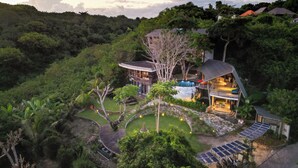 A modern house with a pool, surrounded by lush greenery and hills.