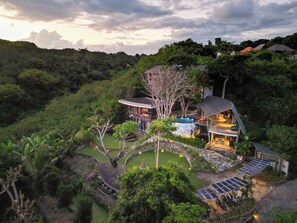 Ein modernes Haus mit Pool, umgeben von üppiger Vegetation und Hügeln.