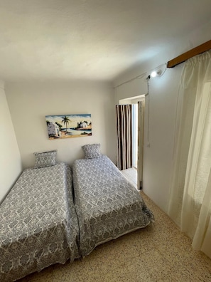 A bedroom with two beds, a painting of a beach scene, a shower, and a curtain.