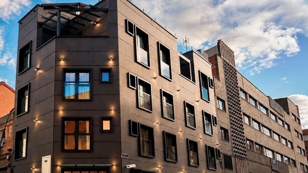 A modern multi-story building with a flat facade, numerous windows, and a car parked in front.