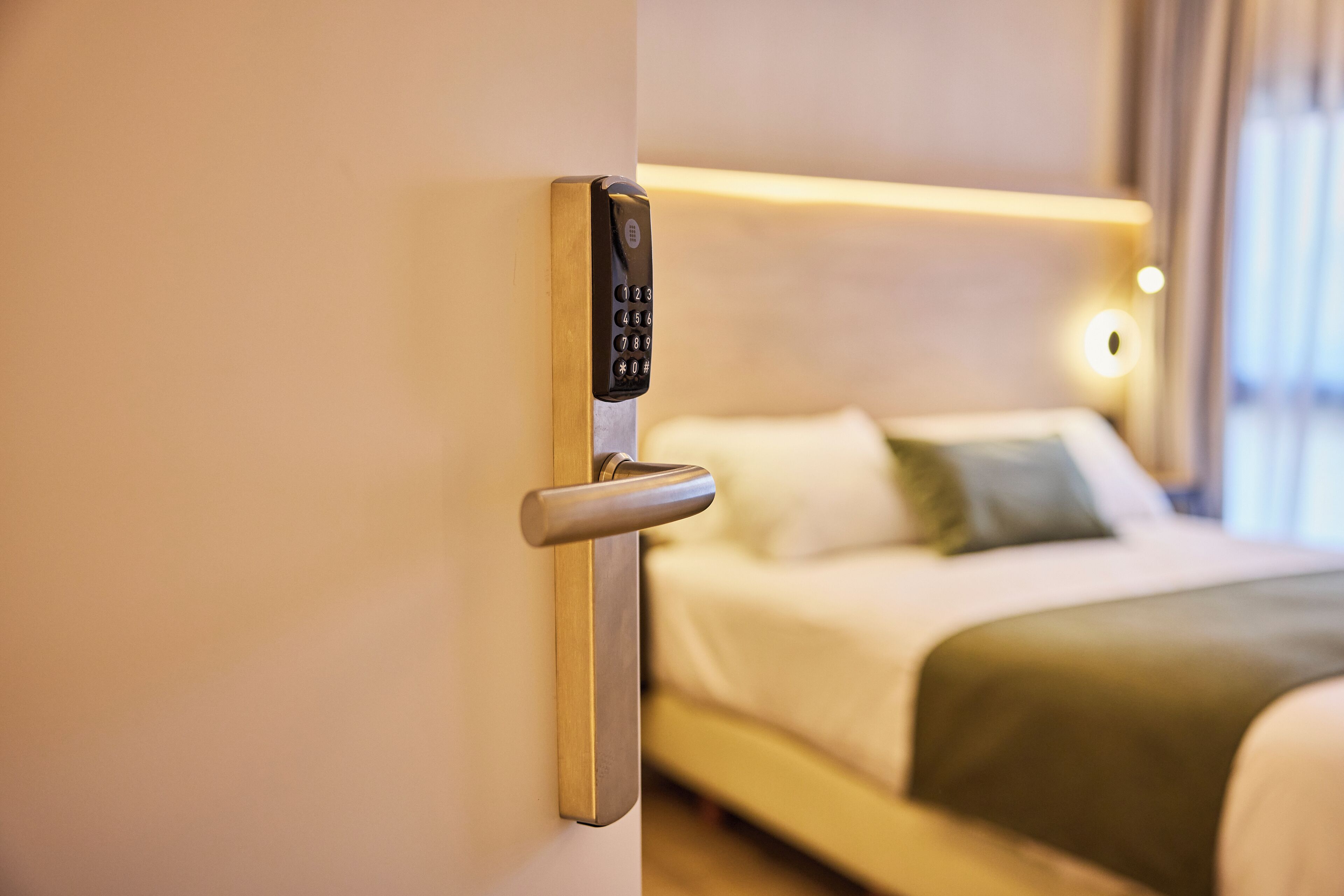 Ein Hotelzimmer mit moderner Türschließanlage, einem Bett mit weißer Bettwäsche und einem Nachttisch.