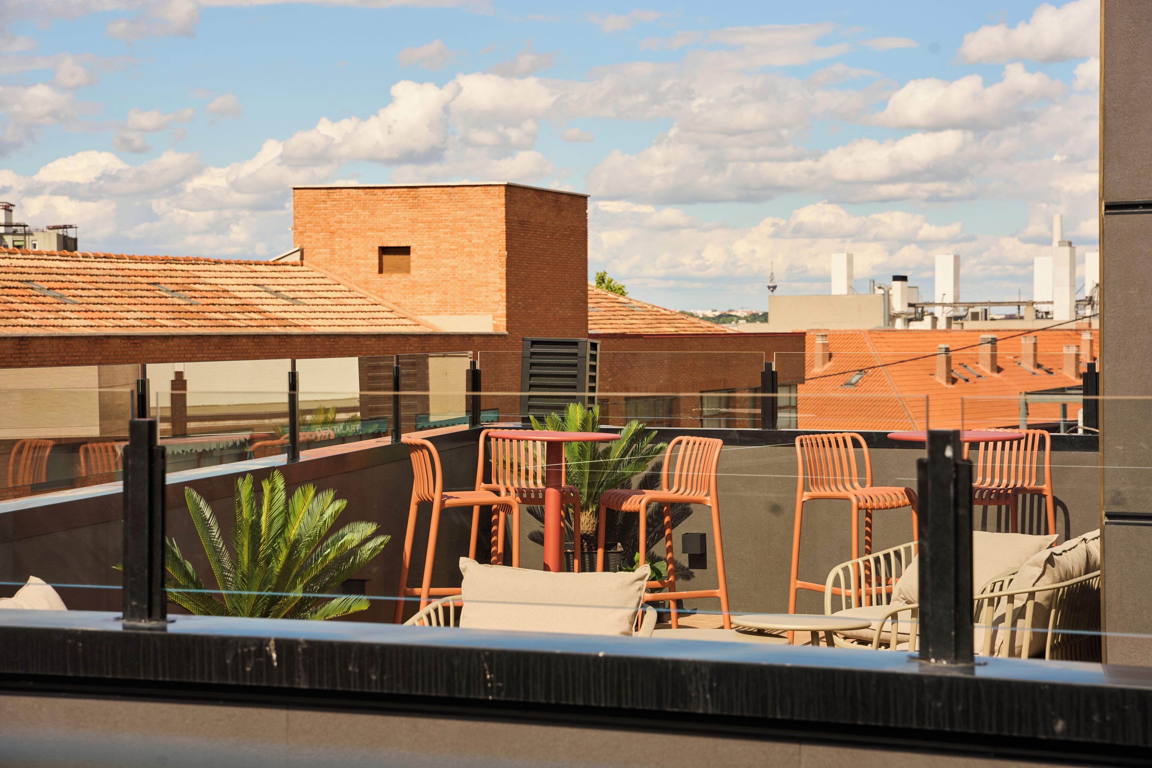 A rooftop terrace with outdoor seating, a brick building, and a clear sky.