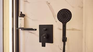 A modern bathroom with a marble wall, a handheld showerhead, and a bottle of shampoo.
