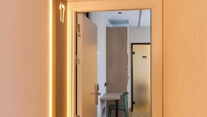 A hallway with a wooden floor, a door with a number, and a view into a room with a table and chairs.