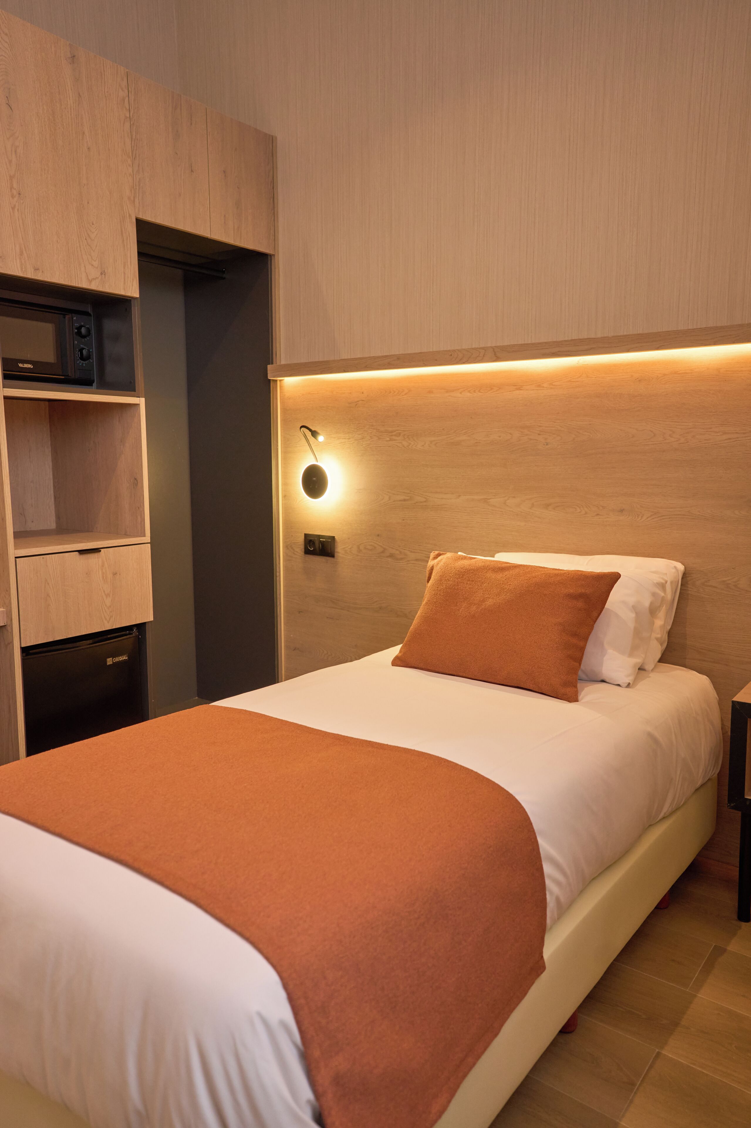 A bedroom with a bed, a nightstand, a built-in wardrobe, and a wall-mounted light fixture.