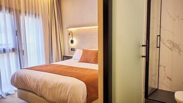 A hotel room with a bed, a nightstand, a wall-mounted lamp, and a shower area.
