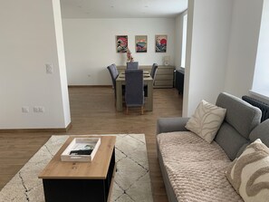 A living room with a sofa, a coffee table, and a dining area with chairs and a table.