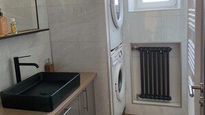 A compact laundry room with a washing machine, a radiator, and a window. - 🌿 Cosy accommodation between nature and tranquillity (Pontpierre)