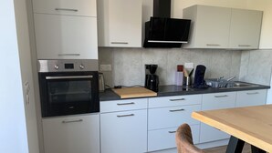 A modern kitchen with white cabinets, a black oven, a microwave, a coffee maker, and a wooden cutting board. - 🌿 Cosy accommodation between nature and tranquillity (Pontpierre)