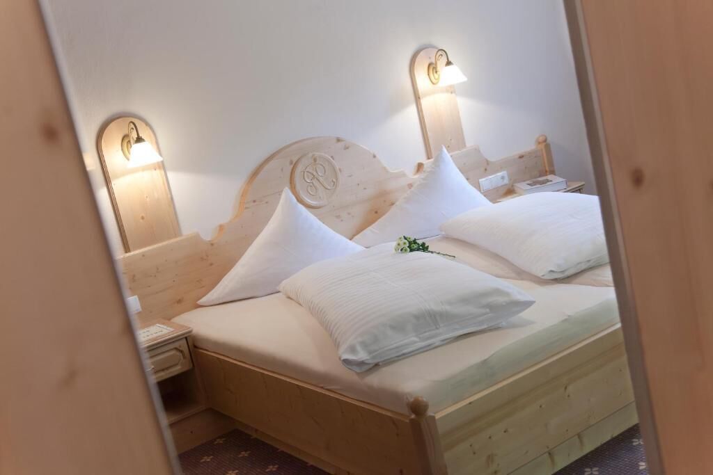 A wooden bed with white bedding and two wall-mounted light fixtures.