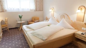 Habitación de hotel con cama, mesitas de noche, una silla, una pequeña mesa con flores y una ventana con cortinas.