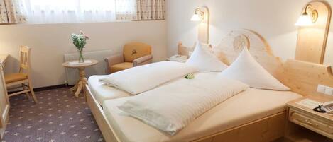 A hotel room with a bed, bedside tables, a chair, a small table with flowers, and a window with curtains.