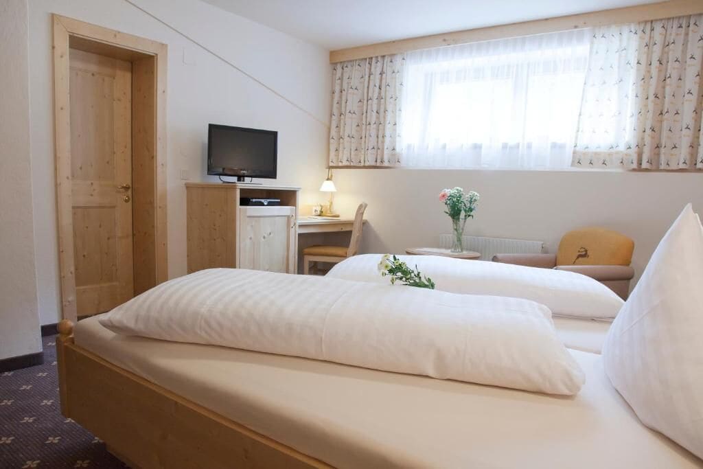 A hotel room with a bed, a desk, a television, and a window with curtains.