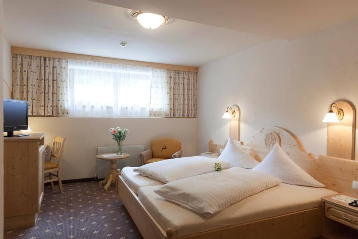 Une chambre d’hôtel avec un lit, un bureau avec un ordinateur, une chaise, une petite table avec des fleurs et une fenêtre avec des rideaux.