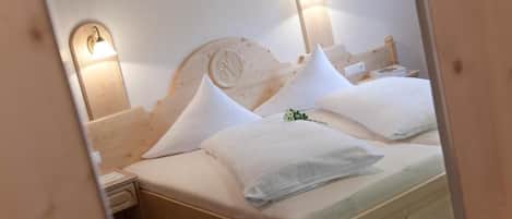 A wooden bed with white bedding and pillows, two bedside lamps, and a nightstand with a lamp.