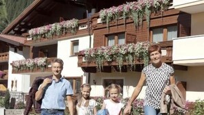 A family walking in front of a building with balconies and flower boxes.