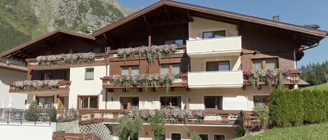Un hotel de varios pisos con balcones decorados con flores, con montañas al fondo.