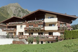 Ein mehrstöckiges Hotel mit Balkonen, die mit Blumen geschmückt sind, vor einer Bergkulisse.