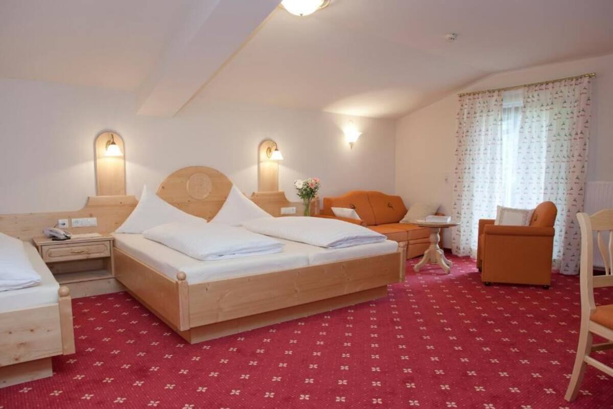 Une chambre d’hôtel avec un lit en bois, une petite table, une chaise et une fenêtre avec des rideaux.