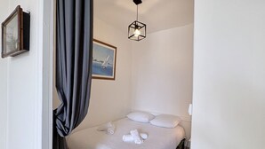 Ein Schlafzimmer mit einem Bett, weißer Bettwäsche, einem Gemälde, einer Pendelleuchte und einem Vorhang.