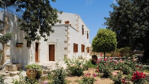 A white building with a stone staircase, surrounded by a garden with various plants and flowers. - Nature’s Peaceful Villa: Pool,BBQ, Fragrant Garden (Rethymno)