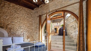 A bedroom with a stone wall, a bed with white bedding, and an open doorway leading to a staircase. - Stone-built cottage with private pool, hot tub and spacious garden! (Rethymno)