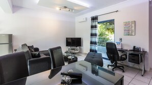 Ein moderner Büroraum mit einem Glastisch, schwarzen Bürostühlen, einem Schreibtisch mit Computer und einem Fernseher.