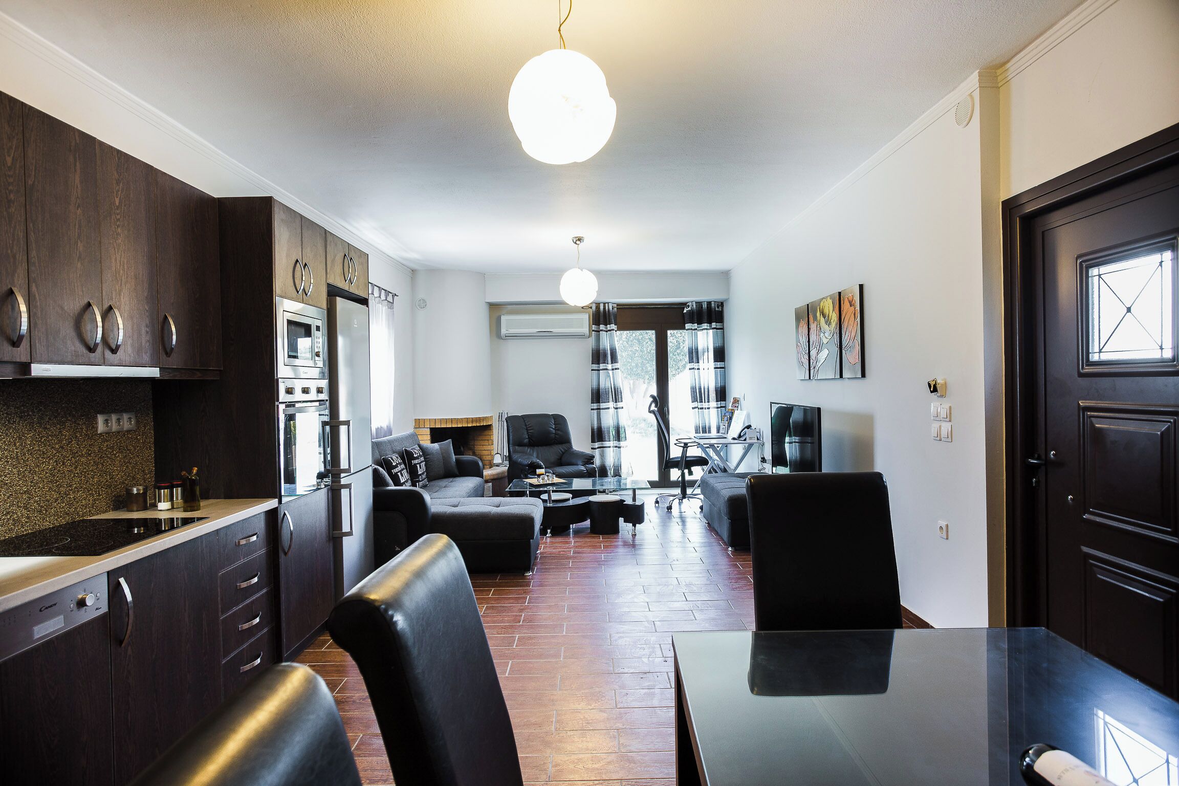 Une cuisine moderne avec des meubles de couleur bois foncé, un îlot central et un coin repas comprenant une table et des chaises noires.