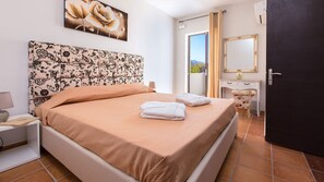 A bedroom with a bed, a nightstand, a lamp, a mirror, and a view of the outdoors. - Close to Sandy Beach & Amenities (Rethymno)