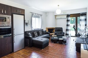 A modern living room with a sectional sofa, a coffee table, a fireplace, and a kitchen area with appliances. - Close to Sandy Beach & Amenities (Rethymno)