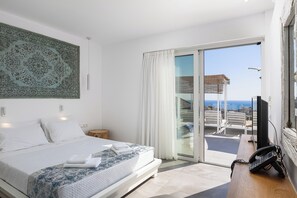 Ein Schlafzimmer mit Bett, Schreibtisch mit Telefon, einem großen Fenster mit Vorhängen und Blick auf einen Balkon.