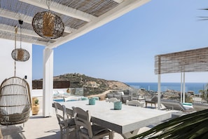 Eine Terrasse mit Tisch und Stühlen, einem Hängesessel und Blick auf das Meer und die Hügel.