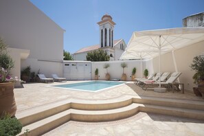 Ein Pool mit Stufen zum Wasser, umgeben von Liegestühlen und Sonnenschirmen.