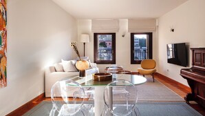 A modern living room with a glass dining table, a sofa, a TV, and a view of the city through large windows. - Charming One-Bedroom Residence in Heraklion Center (Heraklion)